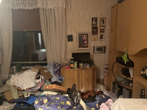 Messiger Raum mit verstreuten Kleidungsstücken und einem Schreibtisch mit Elektronik.