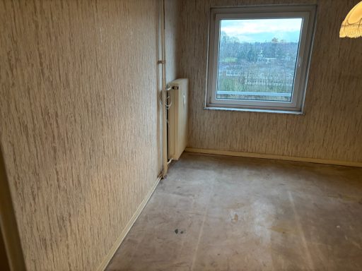 Leerer Raum mit beige gestrichenen Wänden und Fenster mit Blick nach draußen.