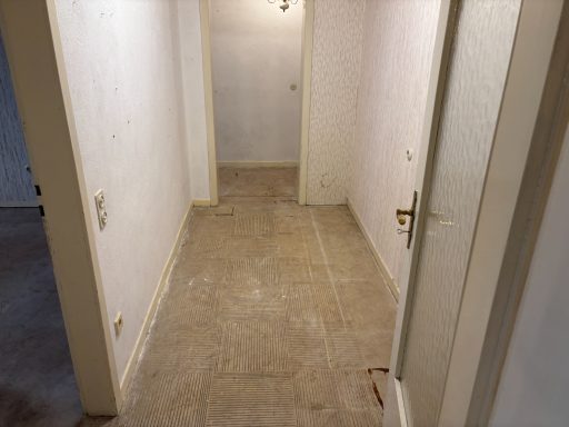 Leerer Flur mit weißen Wänden und hellbraunem Bodenbelag.