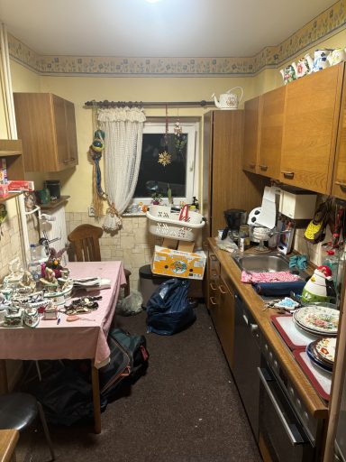 Gemütliche Küche mit Holzschränken, Tisch, Geschirr und unordentlichem Arbeitsbereich.