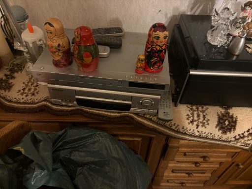 Ein silberner DVD-Player steht auf einer Holzkommode neben Matrjoschka-Puppen und einer Schatulle.