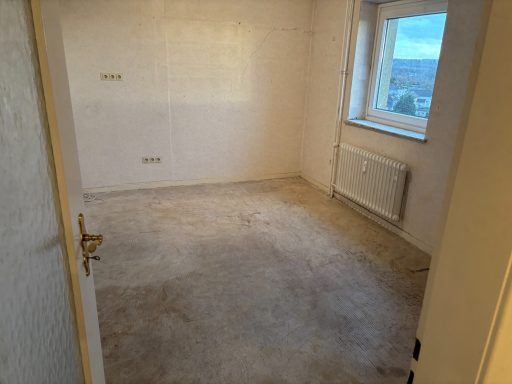 Leeres Zimmer mit Fenster, hellen Wänden und Teppichboden.