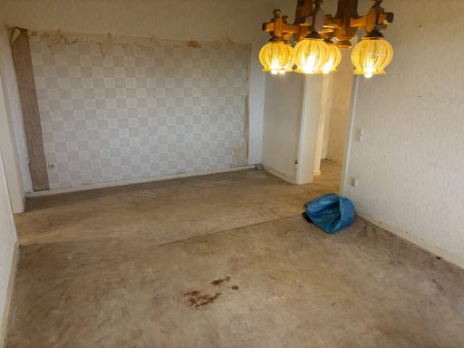 Leere, ungepflegte Wohnung mit abblätternder Wandfarbe und einem blauen Karton auf dem Boden.